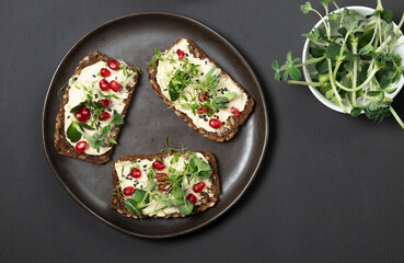 Sandwiches with grain bread, hummus and microgreens. Top view on a black background.