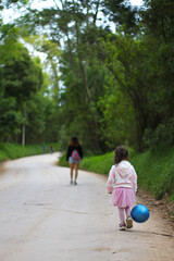 mother and daughter with blue balloon in hand on nature trail with trees and flowers 