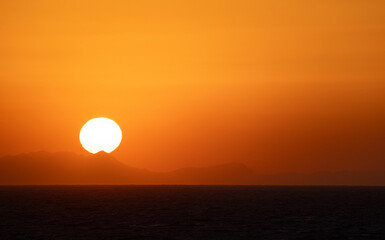 The Sun Falling Behind Mountain peak with sea foreground. A Spectacular golden Sunset 