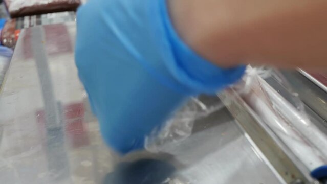 the hands of a merchant in gloves pack a tray with chopped beef basturma with stretch film. Manual thermopacker in action. Retail sale of meat products