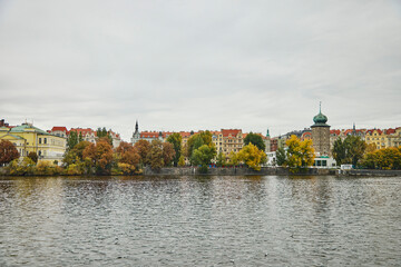 Wide view of architecture in Prague. We see colorful buildings, Vltava river and autumn trees.