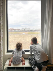 Two young brother looking out window - obrazy, fototapety, plakaty