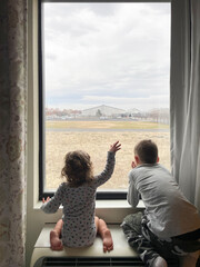 Two young brother looking out window - obrazy, fototapety, plakaty