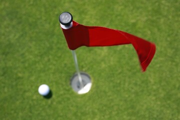 Close up shot of red golf flag and golf ball on golf course putting green shot from above.