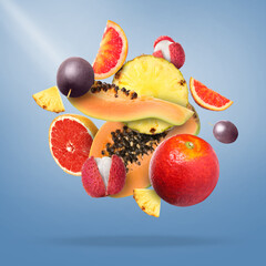 Many fresh tropical fruits falling on pale blue background