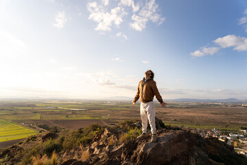 Young man on the top of a mountain taking a deep breath with his head high and arms open feeling the sun, air and wind on his body. Concept of freedom. Copy space on the left.