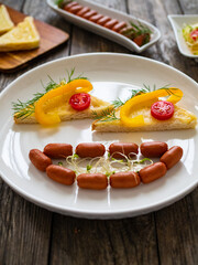 Breakfast - boiled sausages, bread and fresh vegetables served on wooden table
