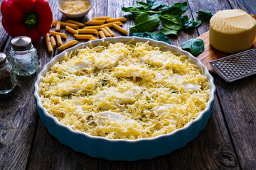 Uncooked noodle casserole with roast pork loin, mozzarella cheese, bechamel sauce and spinach on wooden table


