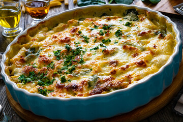 Noodle casserole with roast pork loin, mozzarella cheese, bechamel sauce and spinach on wooden...