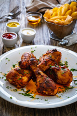 Barbecue chicken drumsticks with French fries on wooden table
