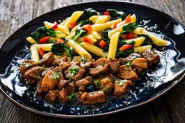 Pasta with roasted pork loin, spinach and parmesan on wooden table

