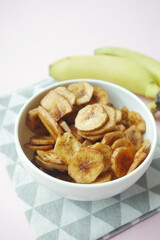  dry banana chips in a bowl on black tiles background 