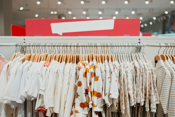 Beautiful baby clothes hanging arranged on rack in a modern store or shop. Shopping interior concept. No people.