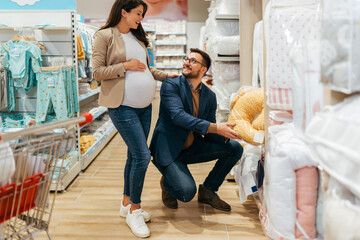 Attractive middle age couple enjoying in buying clothes and bed sheets for their new baby. Heterosexual couple in baby shop or store. Expecting baby concept.