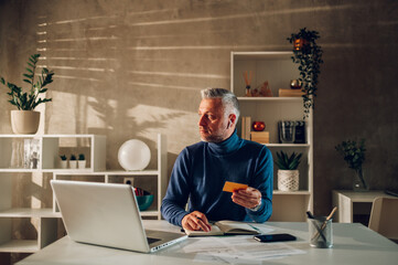 Middle aged man online shopping with laptop and a credit card at home