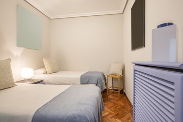 Bedroom with two single beds with white bedspreads, blue blankets, blue painted wooden radiator cover and jatoba parquet floors