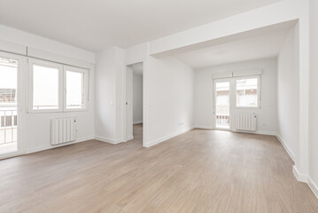 Fototapeta premium Empty living room with laminated flooring and recently finished smooth white walls with access to two similar terraces