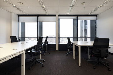 Office tables with black swivel chairs in an office with windows overlooking the city