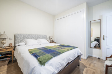 Bedroom with a double bed with an upholstered headboard and a white duvet with a blanket on it, a...