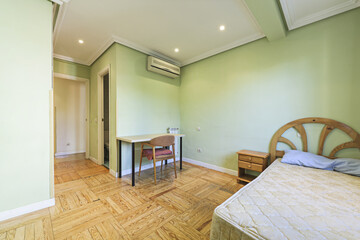 Bedroom with a single bed with a mattress without bedding and a desk with a wooden chair in a room with green walls and plaster moldings