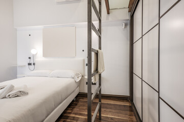 Bedroom with a double bed with a white duvet, dark hardwood flooring, a white upholstered headboard, and a metal ladder