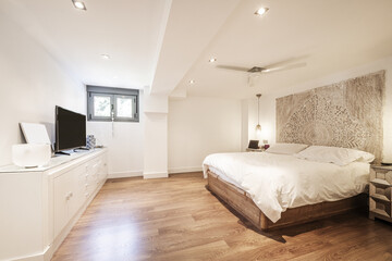 Bedroom with a double bed with a white duvet, dark hardwood floors, a wooden mandala headboard, a...