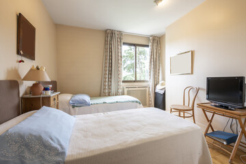 Bedroom with two single beds with white bedspreads, penthouse with thick curtain, folding bamboo table with TV and tall nightstand between the beds