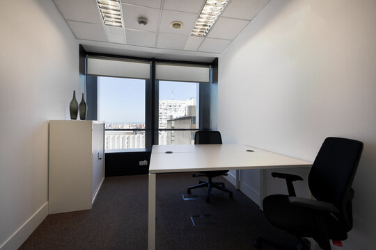 Small office with facing office desks with black swivel chairs in an office with windows overlooking the city