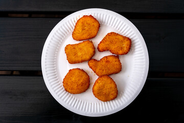 A white plate with a meat dish on a black wooden table. Nuggets on a white disposable plate. Eco-friendly paper tableware. Lunch outside during a picnic.