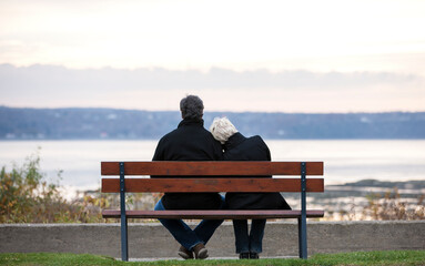 Rear view of mature couple sitting on bench overlooking river in Autumn.