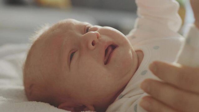 Portrait close-up of a little newborn baby crying and screaming loudly lying on the white bed