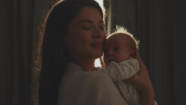 Mother holding her newborn baby in arms and kissing on his baby's forehead in slow-motion 