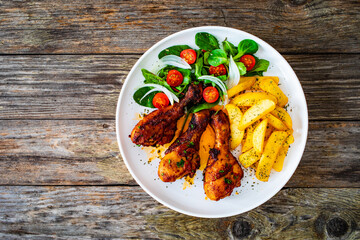 Barbecue chicken drumsticks with french fries, lettuce and mini tomatoes on wooden table
