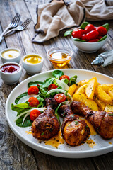 Barbecue chicken drumsticks with french fries, lettuce and mini tomatoes on wooden table
