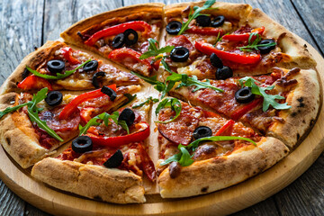 Circle pizza nduja with mozzarella, black olives and arugula leaves on wooden table
