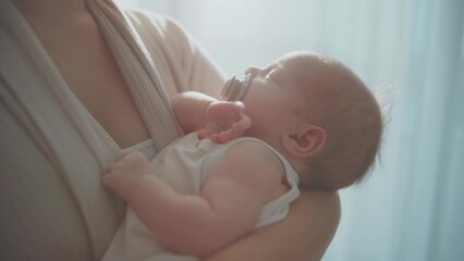 Close-up shot of a cute baby girl sleeping calmly in her mothers arms, baby sucking pacifier while sleeping in slow-motion - Powered by Adobe