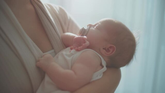 Close-up shot of a cute baby girl sleeping calmly in her mothers arms, baby sucking pacifier while sleeping in slow-motion