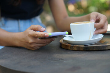 Asian woman looking at earnings on her phone at a coffee shop where she can go to work. amidst green nature