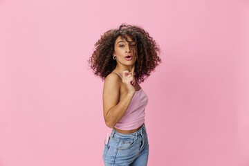 Woman with curly afro hair model poses on a pink background in a pink T-shirt, free movement and dance, look into the camera, smile with teeth and happiness, copy space