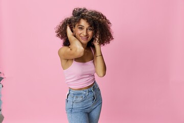 Woman with curly afro hair model poses on a pink background in a pink T-shirt, free movement and dance, look into the camera, smile with teeth and happiness, copy space