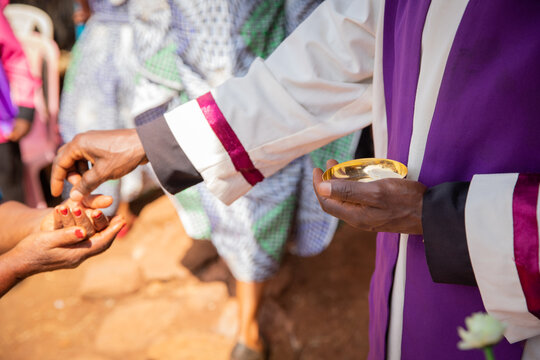 An African priest gives sacramental bread to a believer, focus on the hand with sacramental bread.