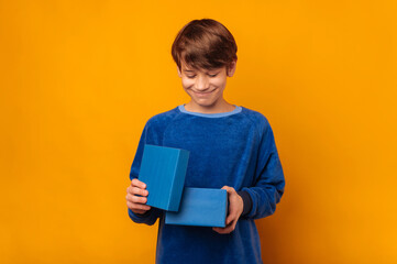 Studio portrait of a young shy smiling boy who opens a blue gift box .