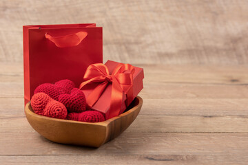 Red knitted hearts and gift box in a wooden bowl in the shape of a heart and gift package on a wooden background. Happy Valentine's Day, Mother's Day and birthday greeting card.