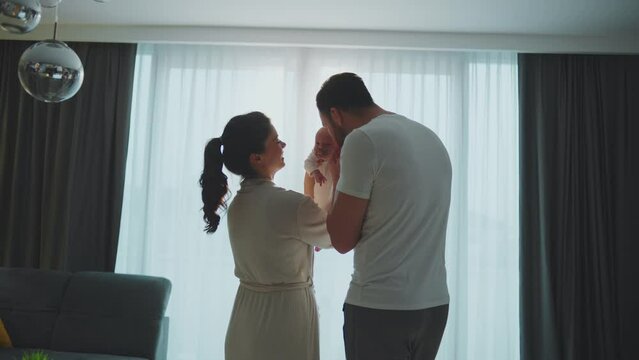 Slow-motion shot of young father and mother holding their baby on hands, caressing their cute newborn baby daughter. Parents expressing unconditional love
