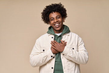 Happy pleased excited grateful African American teen guy holding hands on chest expressing...