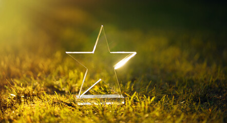 Transparent five-pointed star made of glass on a green summer background. The winner's prize is in...