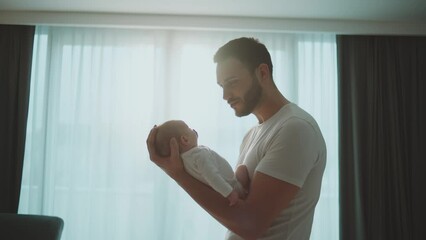 Young bearded father holding his newborn baby in arms, looking and smiling at the baby in slow-motion - Powered by Adobe