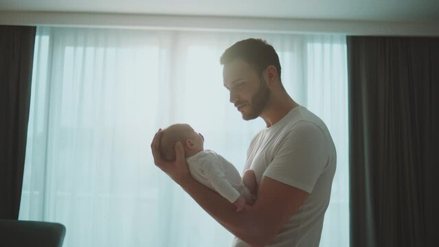 Young bearded father holding his newborn baby in arms, looking and smiling at the baby in slow-motion