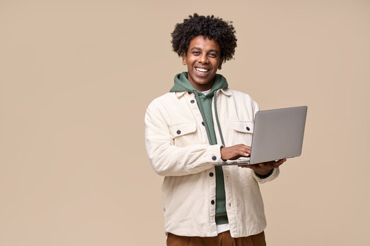 Young happy cool African American teenager student boy holding laptop using computer technology advertising elearning remote education and online webinars isolated on light beige background.