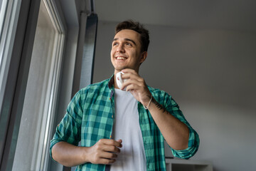 Man standing by the window with cup of coffee in morning daily routine